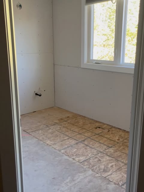 Bathroom renovation in progress, with plasterboard walls and exposed subfloor